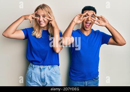 Young interracial couple wearing casual clothes doing peace symbol with fingers over face, smiling cheerful showing victory Stock Photo
