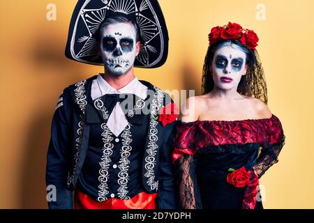 Young couple wearing mexican day of the dead costume over yellow looking sleepy and tired, exhausted for fatigue and hangover, lazy eyes in the mornin Stock Photo