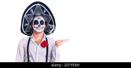 Man wearing day of the dead costume over background smiling cheerful presenting and pointing with palm of hand looking at the camera. Stock Photo