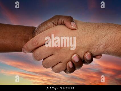Handshake between two hands with different colors on a amazing sky of background Stock Photo