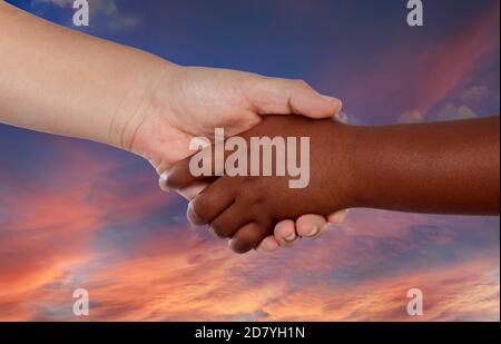 Handshake between two hands with different colors on a amazing sky of background Stock Photo