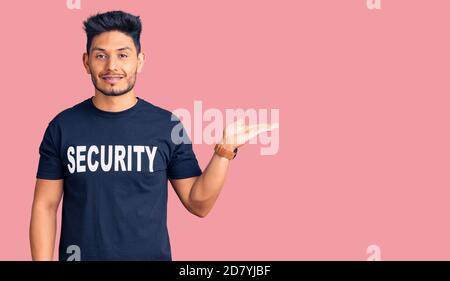 Handsome latin american young man wearing security t shirt smiling cheerful presenting and pointing with palm of hand looking at the camera. Stock Photo