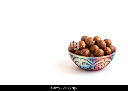 clay bowl with macadamia nuts in shell on white background, copy space Stock Photo