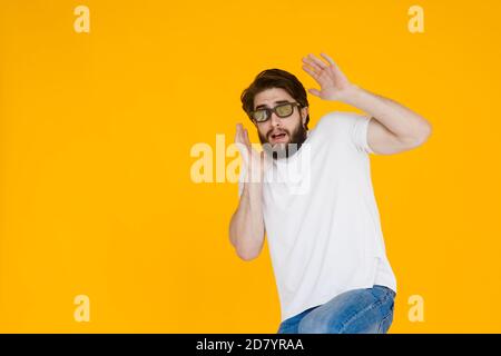 Portrait of a shaggy, bearded scared man in 3D glasses with an open mouth and big eyes, on a yellow background. Stock Photo