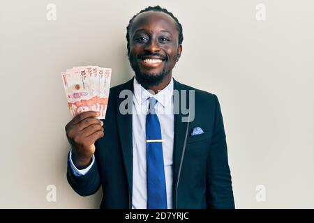 Handsome young black man wearing business suit holding 10 colombian pesos looking positive and happy standing and smiling with a confident smile showi Stock Photo