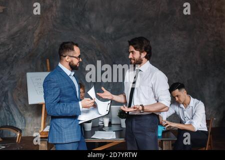 Diverse friendly male partners colleagues talking walking in modern office hallway, young african american and caucasian business men discussing Stock Photo