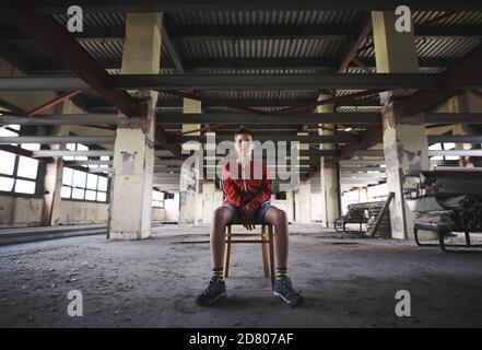 Sad and disappointed teenagers boy sitting indoors in abandoned building. Stock Photo