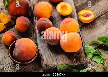 Peaches with leaves on wooden table with peach in halves. Ripe juicy peaches. Harvest of peaches for food or juice. Fresh organic fruit. Stock Photo