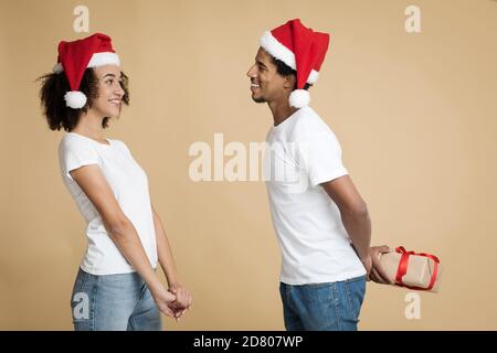 Happy young couple celebrating New year and Christmas on party. African american man in hat with smiling holding box Stock Photo