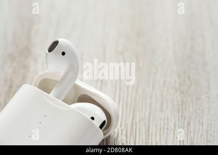 White wireless headphones in a charging case on a wooden background. Stock Photo