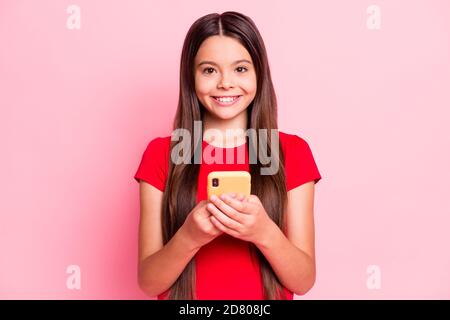 Photo of charming cute little lady long hairdo hands hold telephone chatting typing sending email surf internet shiny smile wear casual red t-shirt Stock Photo