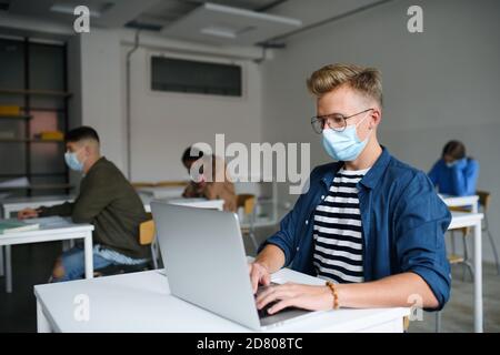 Young students with face masks at desks at college or university, coronavirus concept. Stock Photo