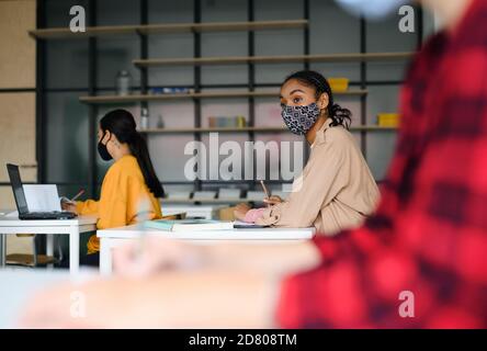 Young students with face masks at desks at college or university, coronavirus concept. Stock Photo