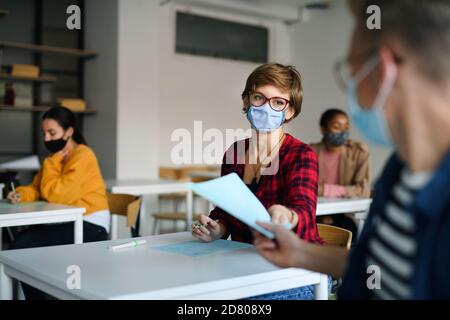 Young students with face masks at desks at college or university, coronavirus concept. Stock Photo