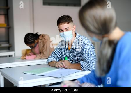 Young students with face masks at desks at college or university, coronavirus concept. Stock Photo