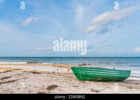 small green boat on empty sand beach against sea and blue sky Stock Photo