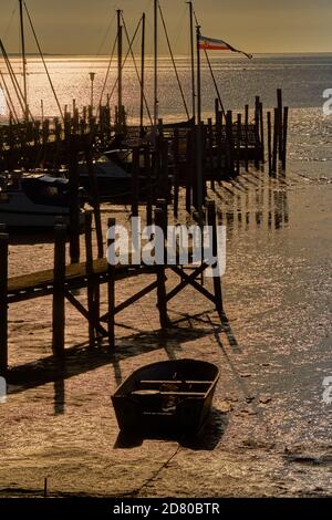 Port with a wooden ship mooring in the Wadden Sea of the North Sea at sunrise with a rowing boat on the beach Stock Photo