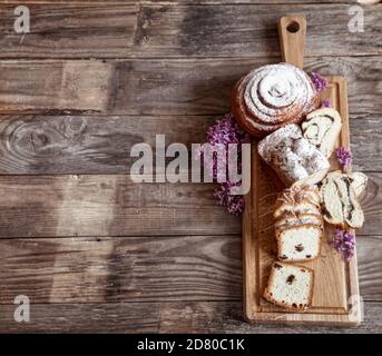 Different fresh pastries are cut on a wooden stick, decorated with lilac blooms. Stock Photo