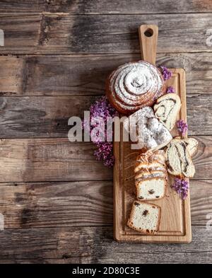 Different fresh pastries are cut on a wooden stick, decorated with lilac blooms. Stock Photo