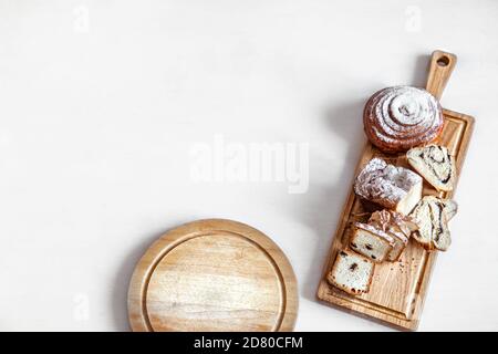 Different fresh pastries are cut on a wooden stick . On a light background, space for text. Stock Photo