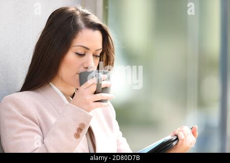 Businesswoman drinking coffee and reading inform standing in the street Stock Photo