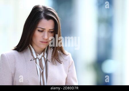 Sad woman complaining walking in the street looking down Stock Photo
