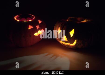 two Halloween pumpkins, turned to each other frightening faces, glowing in the dark with red and yellow mesmerizing light Stock Photo