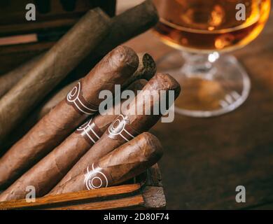 Cigars, luxury smoking concept. Cuban cigars in a wooden box, blur glass of cognac brandy, closeup view with details, copy space Stock Photo