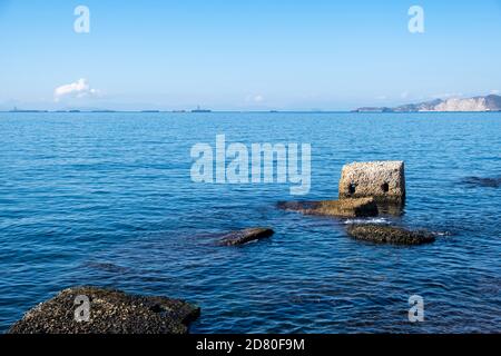 Drapetsona old harbor, Piraeus, Greece. Old structure of stone mooring bollards in the water. Moored cargo ships, boats and vessels. Blue sky and sea Stock Photo