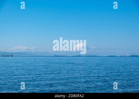 Drapetsona old harbor, Piraeus, Greece. Cargo ships and boats. View from beach of moored vessels. Blue sky and clear calm sea a sunny day. Stock Photo