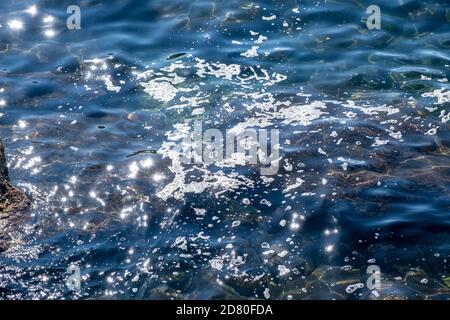 Sea pollution concept. Foam on the sunny water surface, oil, petroleum, chemicals. No place for life is the result of damage to the environment. Stock Photo