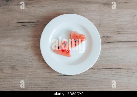 Watermelon 2 slices in the shape of a heart on a white plate on a wooden background. Stock Photo