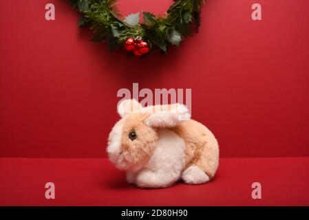 small stuffed toy rabbit isolated on a red background under a Christmas garland Stock Photo