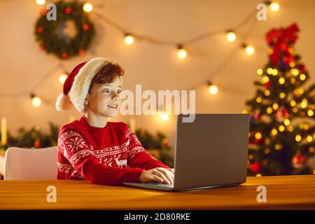 Boy sitting in a room with Christmas decor in front of a laptop with a surprised expression on face. Stock Photo