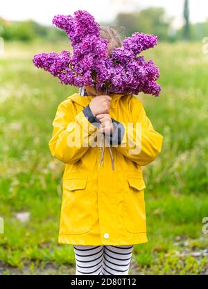 Little lovely girl with a bouquet of lilacs sitting on a bench in the ...