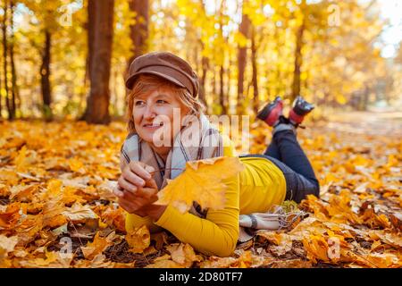 Fall activities. Woman lying on heap of leaves in autumn park. Senior woman having fun outdoors Stock Photo