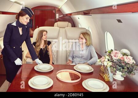 Air hostess inside airplane serves first class passengers. Stock Photo