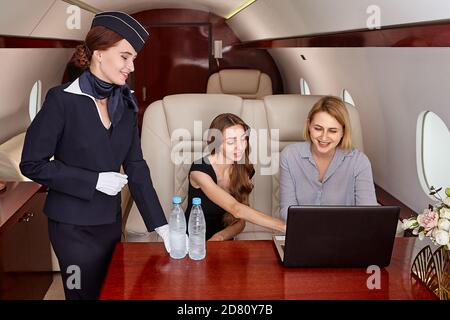 Flight attendant inside airplane serves business class passengers. Stock Photo