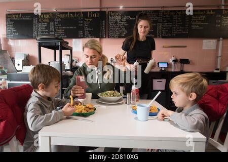 RETRANSMITTING ADDING NAMES Leigh Anderson, with her sons Charlie Brown (left) and Albie Brown, eat a meal at the Kitchen cafe in Bermondsey, London, are providing free school meals for children over the half term holidays. Local councils and businesses are continuing to pledge free food for children in need during this week's half term break after the Government defeated a Labour motion to extend free school meals provision in England over the holidays. Stock Photo