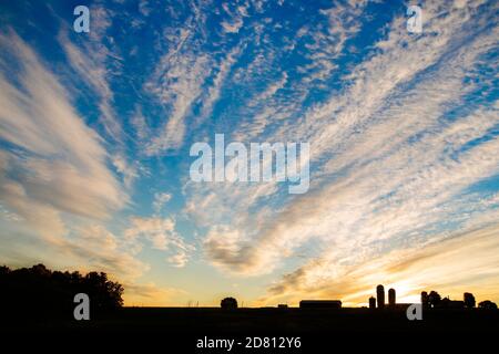Dramatic clouds are illuminated at sunrise above Vermont Farm Stock Photo
