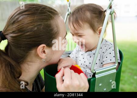 Mother Smiles at Happy Daughter While Playing Outdoors on Swingset Stock Photo