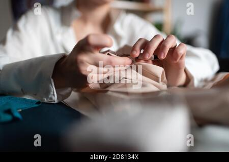 Closeup of faceless female designer ripping stitches of sewed clothes using seam ripper having small home business Stock Photo