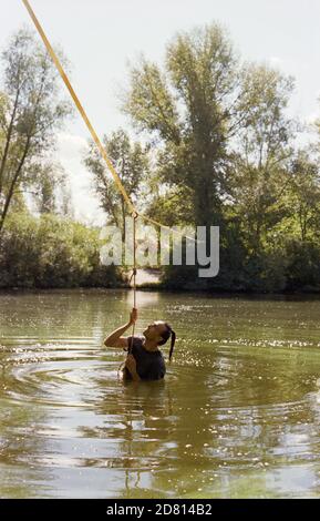 A man practicing slackline over a river in the forest at sunset. Stock Photo