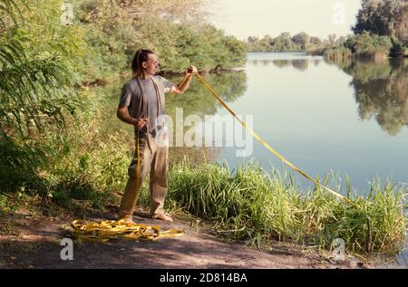 A man sets a slackline over a river in the forest at sunset. Stock Photo