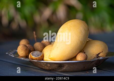 Background with a plate of tropical fruits on a wooden table. Yellow mango and lychee. Close up. Stock Photo