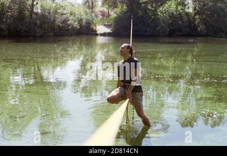 A man practicing slackline over a river in the forest at sunset. Stock Photo