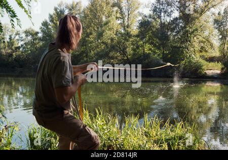 A man sets a slackline over a river in the forest at sunset. Stock Photo