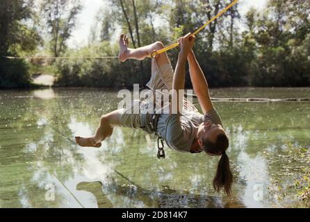 A man practicing slackline over a river in the forest at sunset. Stock Photo