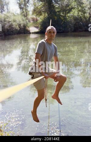 A man practicing slackline over a river in the forest at sunset. Stock Photo