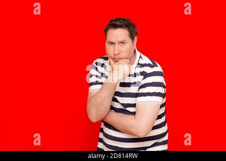 Middle age american man wearing striped t-shirt over isolated red background with hand on chin thinking about question Stock Photo
